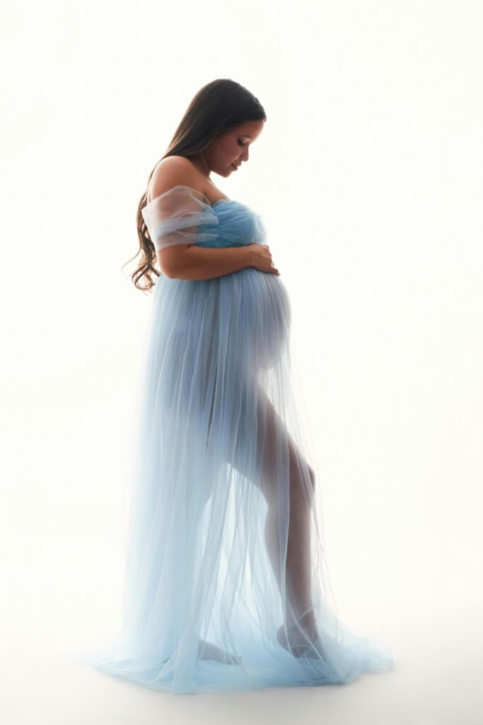 Elegant maternity portrait with soft lighting and flowing blue gown, showcasing beauty of pregnancy.