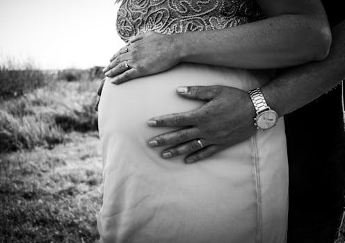 Close-up shot of hands embracing a pregnant belly in black and white outdoors.