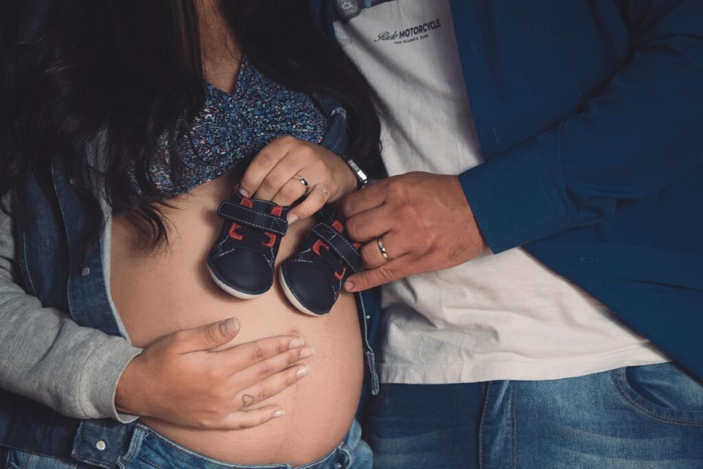 A pregnant couple showing their newborns shoes.