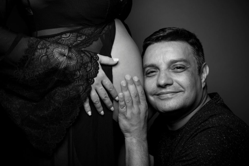 A loving expectant father embraces his partner's baby bump in a monochrome portrait.