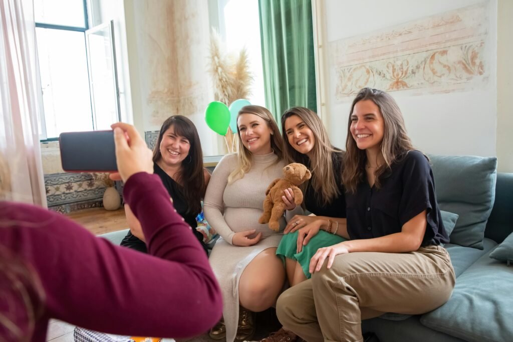 Four women enjoying a joyful baby shower indoors, smiling and posing for photos.